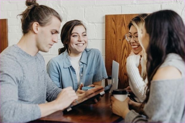 Cuatro personas jóvenes conversando y riendo alrededor de una mesa de madera